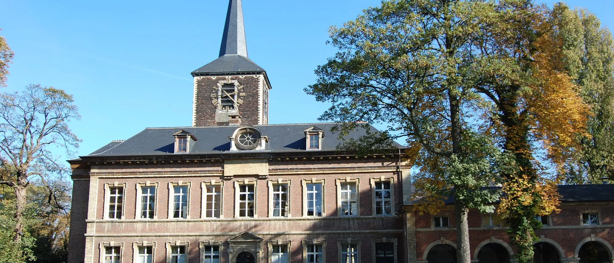 La façade et le clocher de l'abbaye de Forest entourés d'arbres