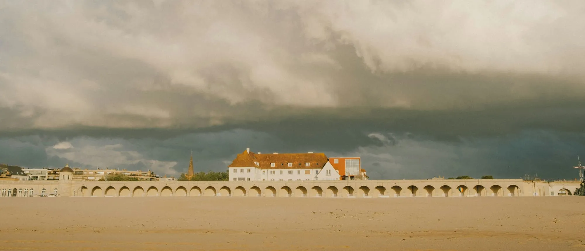 Het strand van Oostende met de Koninklijke Gaanderijen en het Thermae Palace onder een wolkenlucht
